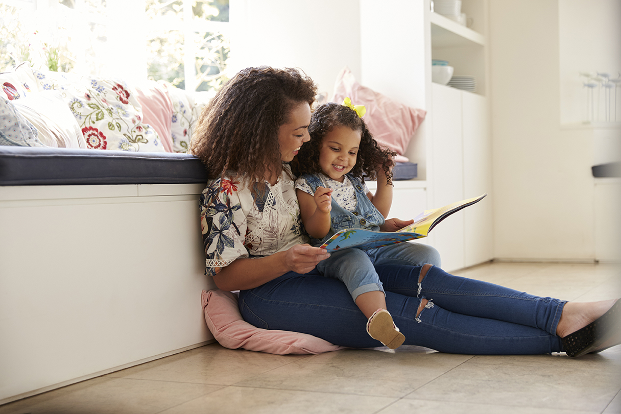 a mother sitting with her daughter reading a book together