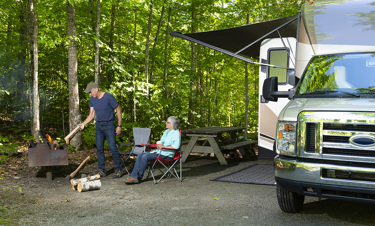 Senior couple enjoying the outdoors with camp chairs and fire and recreation vehicle