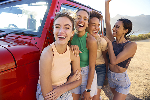 happy friends standing outside vehicle