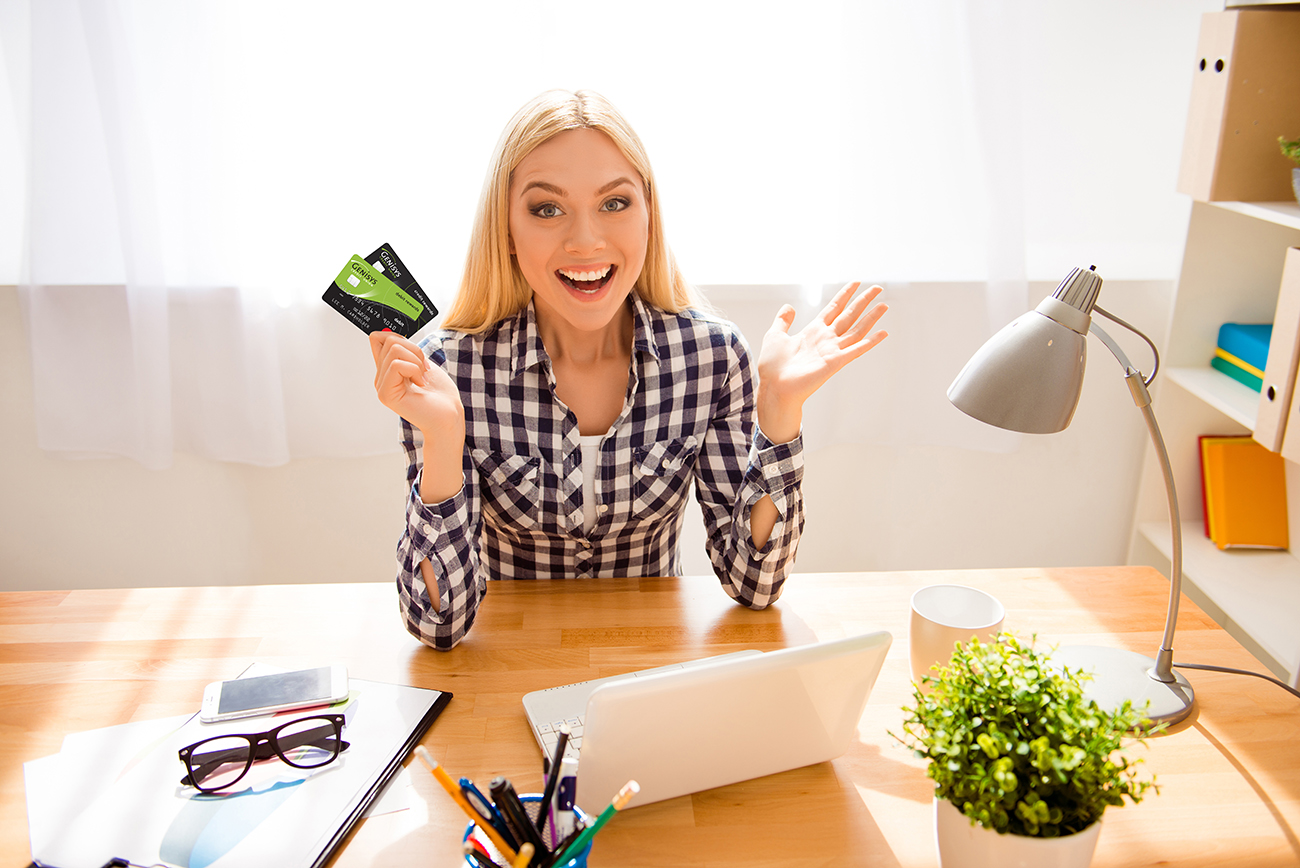 Woman sitting at desk holding Genisys Debit and Credit Mastercard