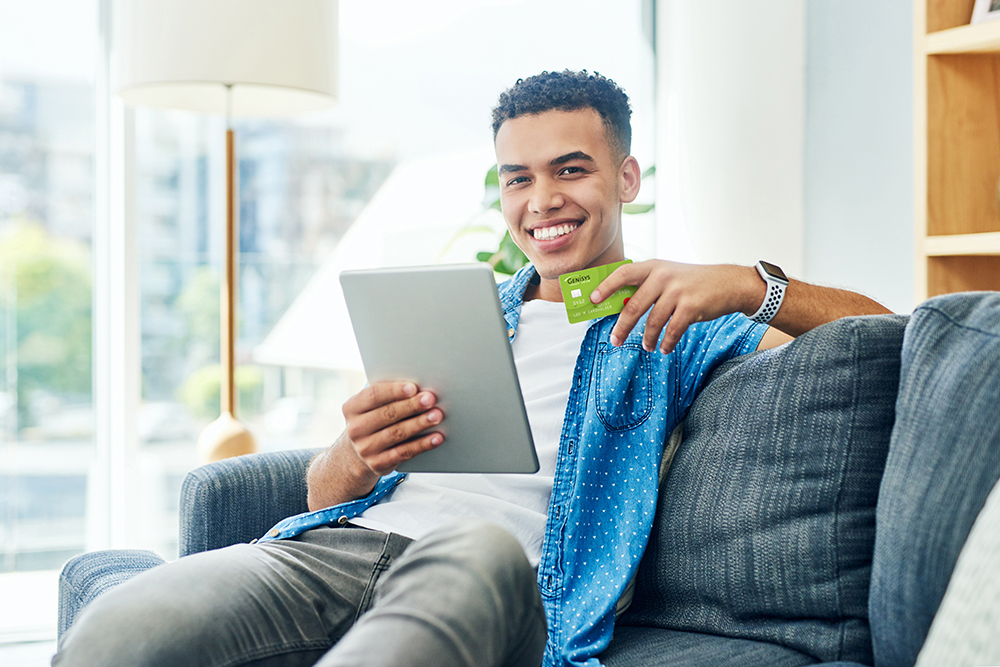 man holding Genisys Debit Rewards Mastercard while using a tablet