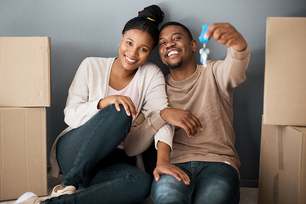 couple sitting on floor with moving boxes, smiling and holding new house keys