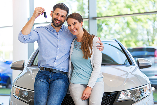 happy couple holding car keys at car dealership