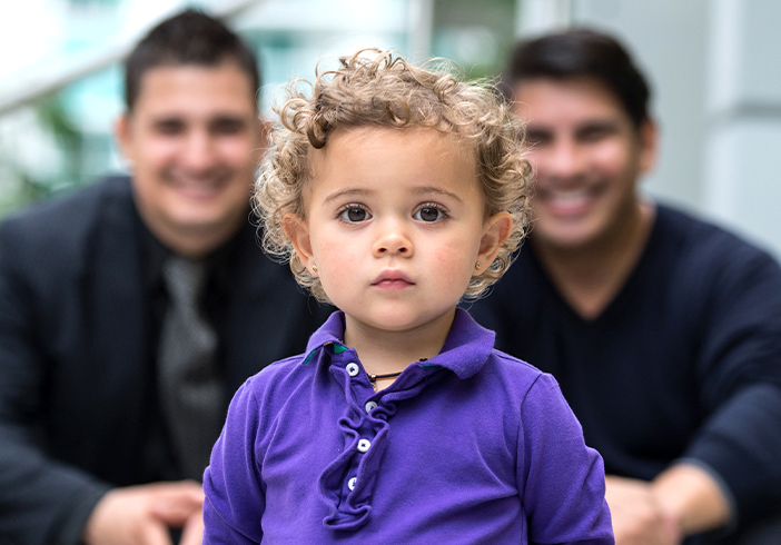 Curly haired toddler standing in front of adoptive fathers