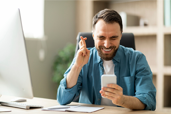 Man with fingers crossed for good luck holding phone