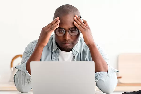 Man with hands on his head looking at his laptop