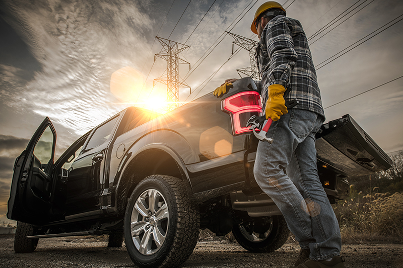 man holding hammer and wrench near the tailgate of a black work pick up truck
