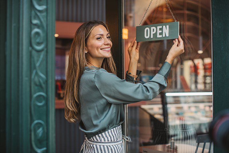 Business owner standing at entrance to her shop displaying an open sign