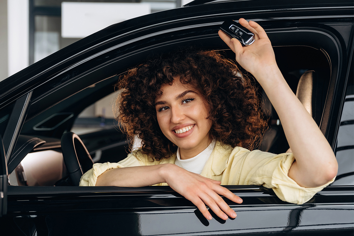 Woman sitting in drivers seat of car holding keys out the window and smiling