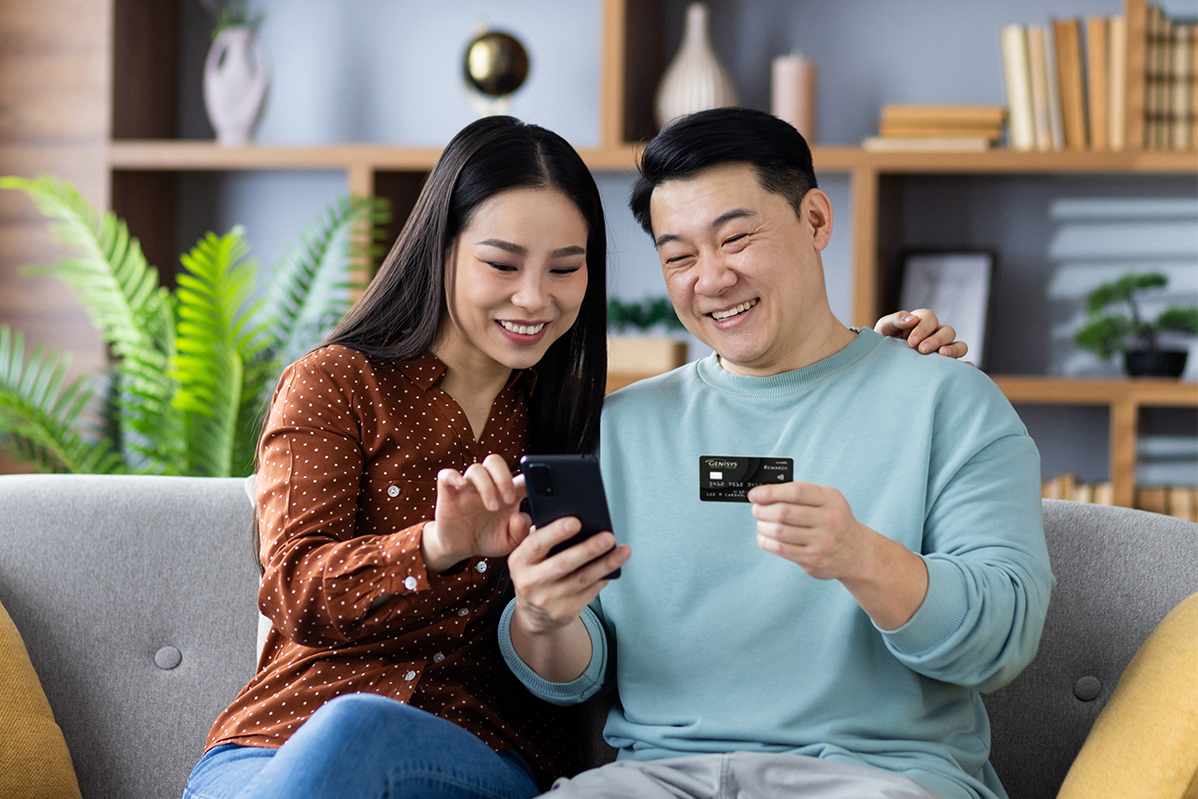 Couple sitting on their couch using their Genisys Rewards Mastercard online