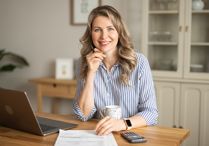 Woman sitting at a table with documents, a calculator, and laptop