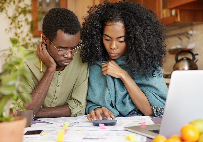 Couple sitting at a table looking at bills and using a calculator