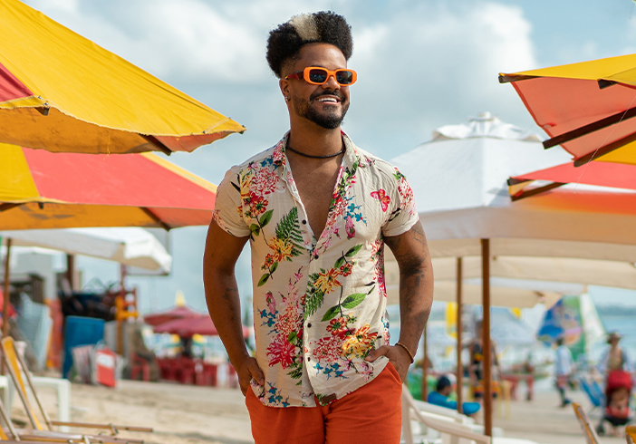 Man in sunglasses walking on the beach passing by beach chairs and umbrellas