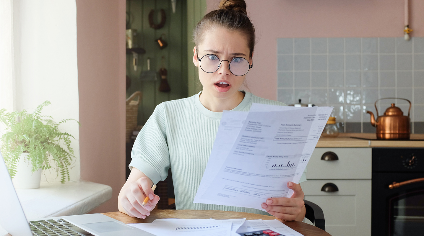 Woman sitting at kitchen table holding bill statements looking concerned